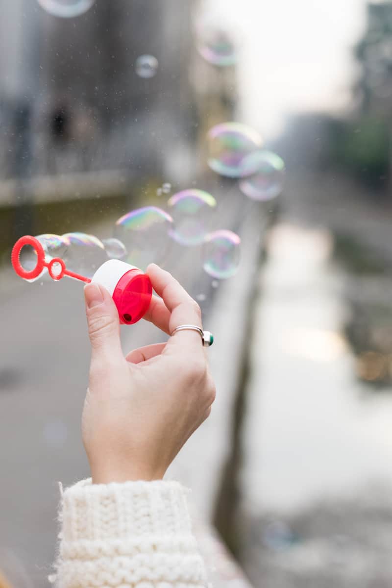 how to make bubbles and a Hand holding a red bubble wand with bubbles floating through the air