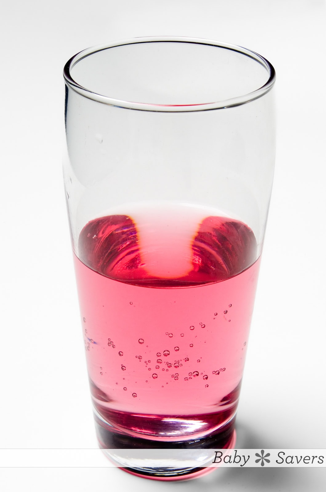 A clear glass filled with homemade pedialyte clear pink liquid, showcasing bubbles. The glass sits against a white background with the site logo, "baby savers"  printed at the bottom.