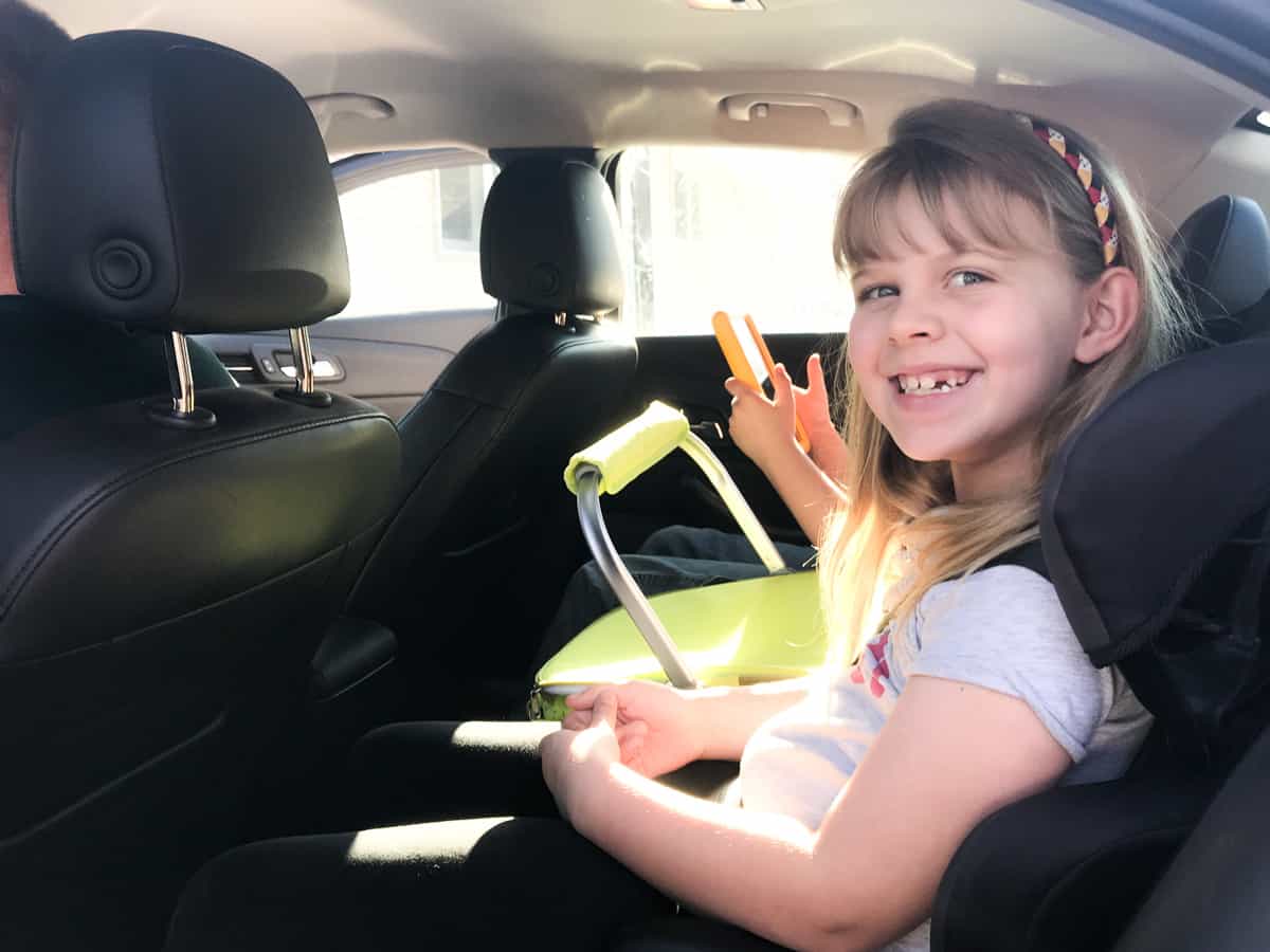 Smiling in the backseat of a car next to a basket of road trip essentials