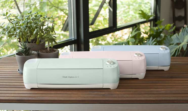 Mint green, pink and blue Cricut Explore Air 2 machines on a wood slatted table