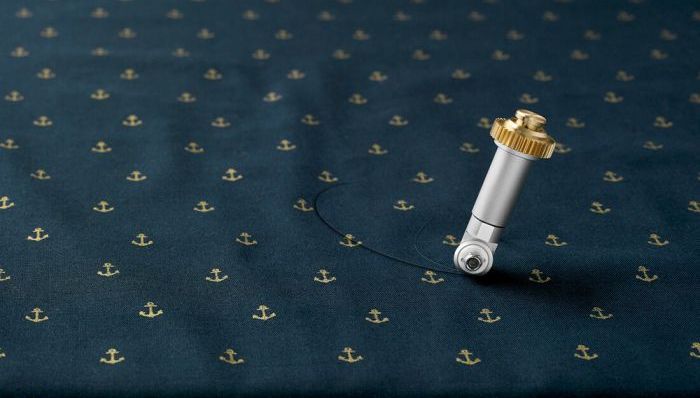 Cricut maker rotary fabric blade cutting navy fabric with gold anchors on it.