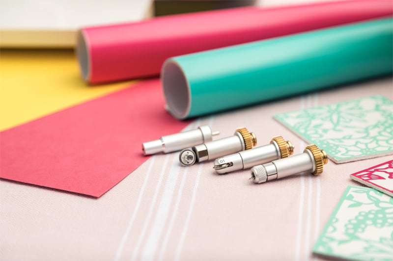 Vinyl in yellow, pink and green behind various cutting and scoring blades