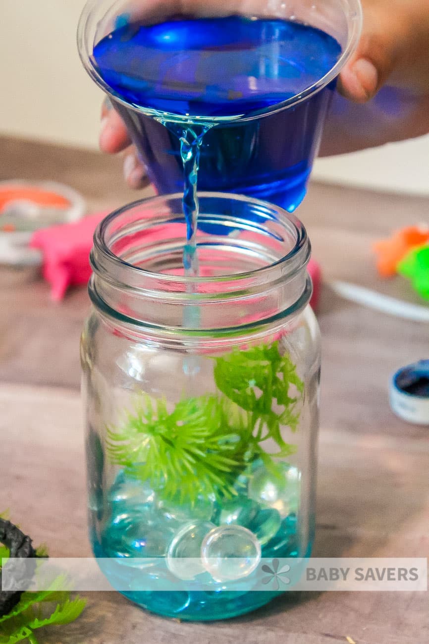 pouring blue water into homemade mason jar aquarium