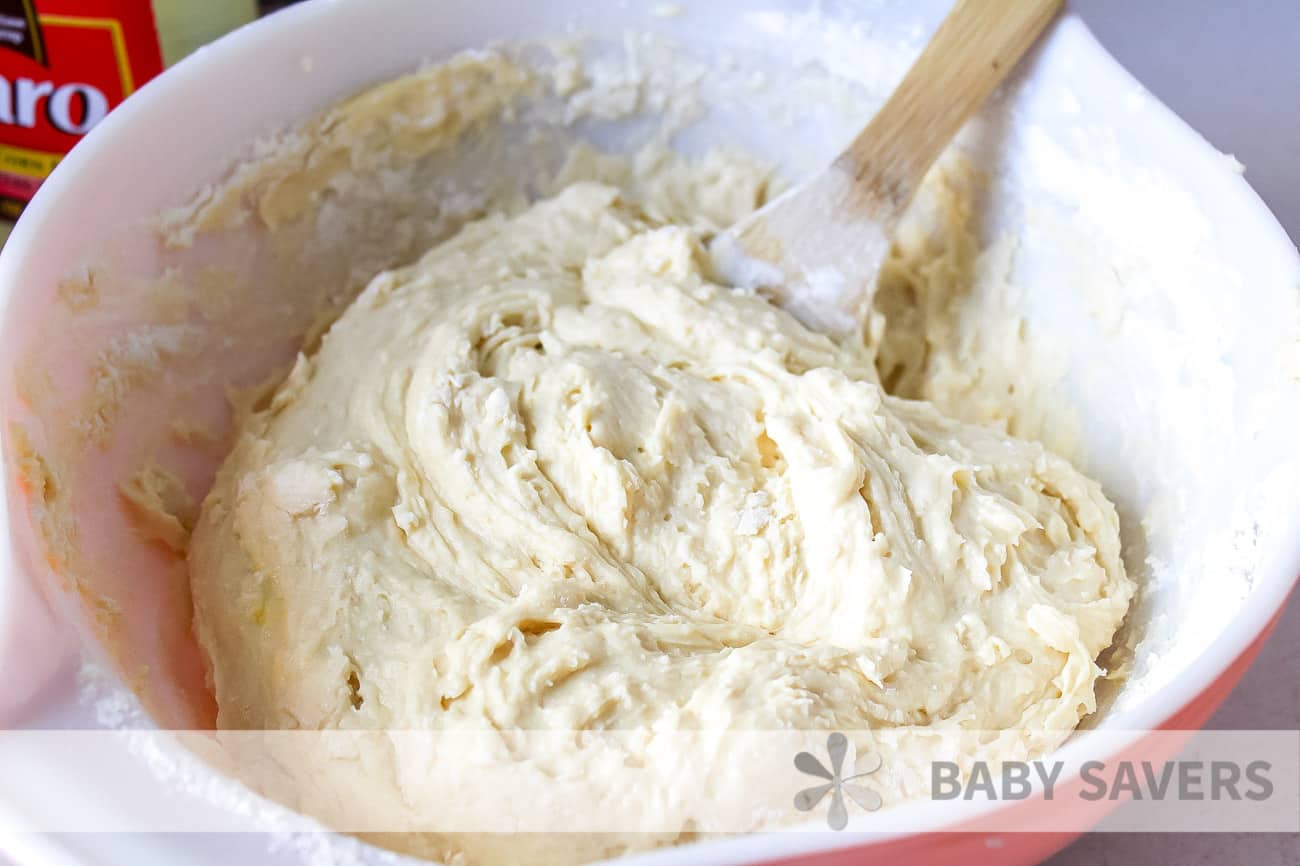 White mixing bowl with wooden spoon stirring dough