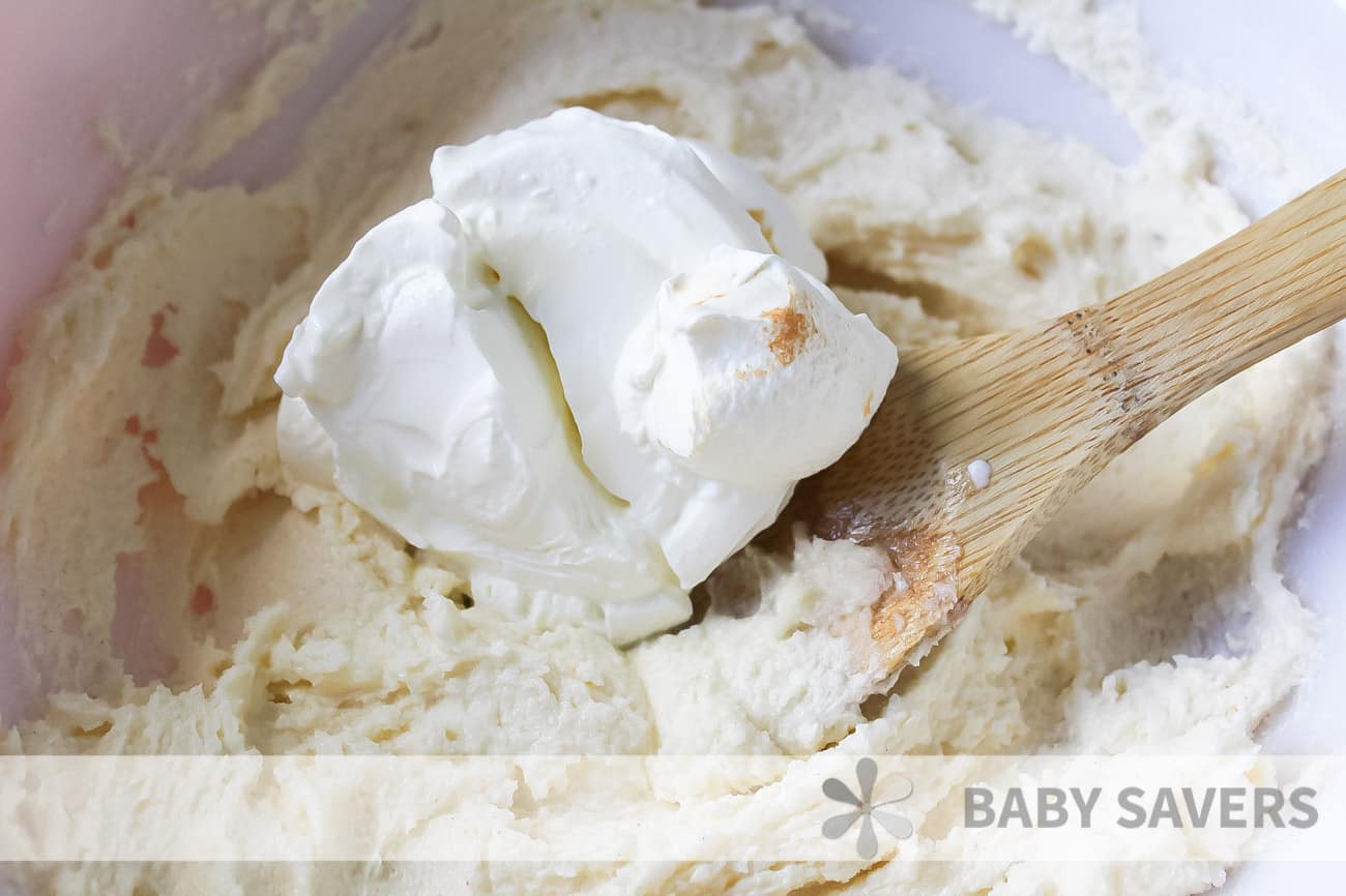 Whipped cream being stirred into a cream mixture with a wooden spoon