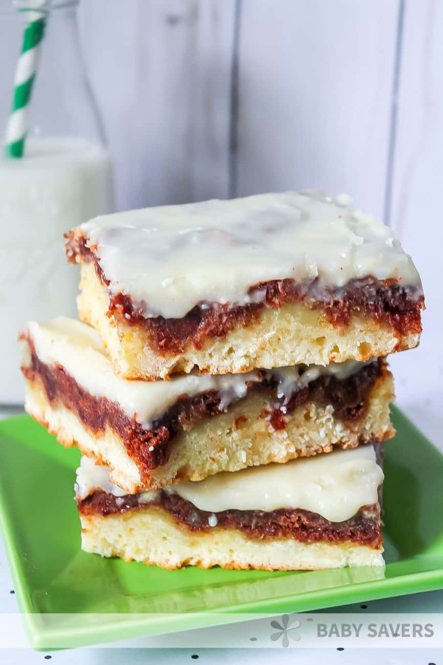 a green plate with a stack of three frosted dessert bars stacked on top