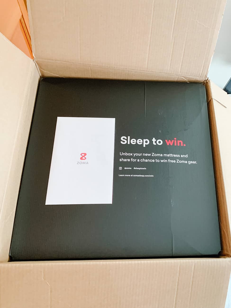 Top of the box from a Zoma mattress with text reading Sleep to Win