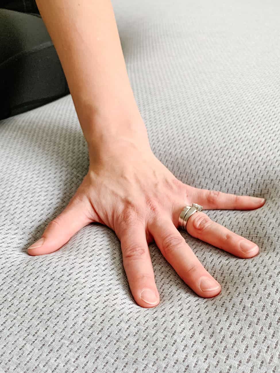 woman's hand with rings pressed into a grey mattress