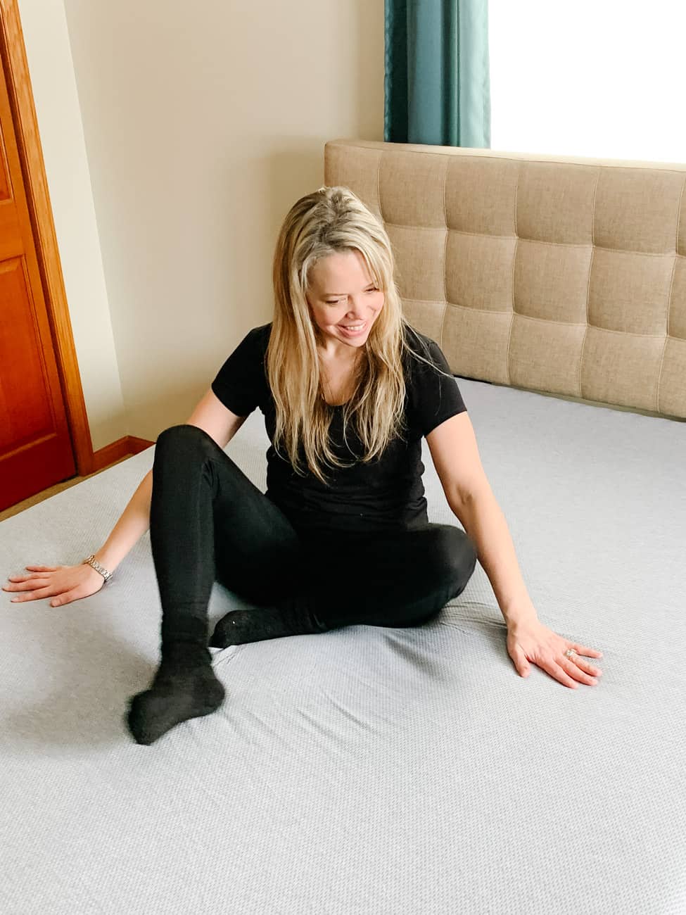 smiling woman sitting on a zoma sports mattress with a grey cover