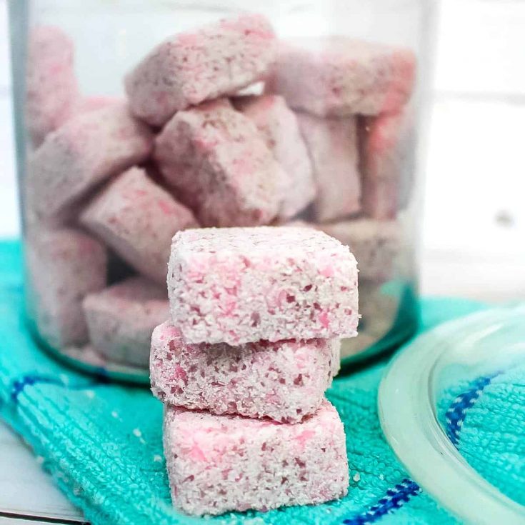 pink diy laundry detergent pods stacked up in front of a glass jar with more detergent in it