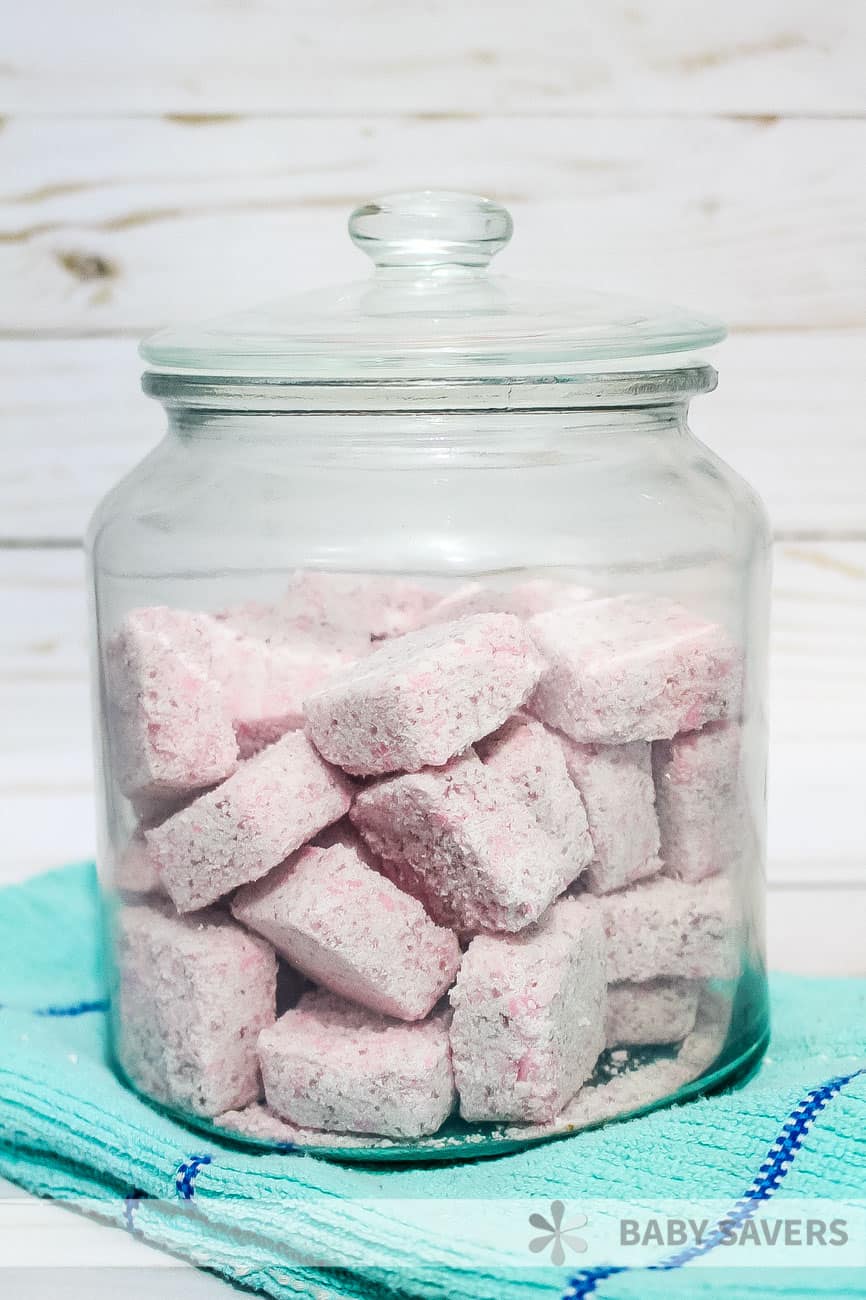 pink cubes of homemade laundry detergent in a glass jar on an aqua kitchen towel