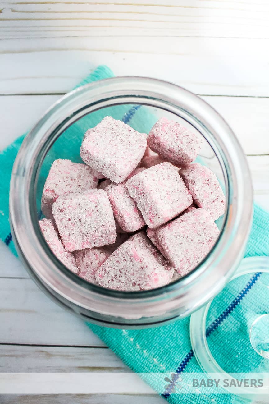 pink pods of diy laundry detergent in glass jar on a green towel