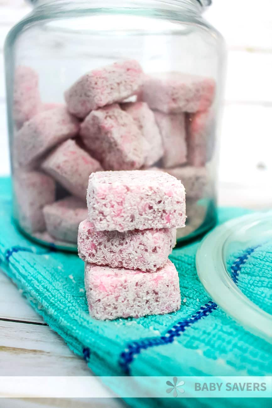 Stack of pink tablets of DIY laundry detergent in front of a glass jar full of more tabs