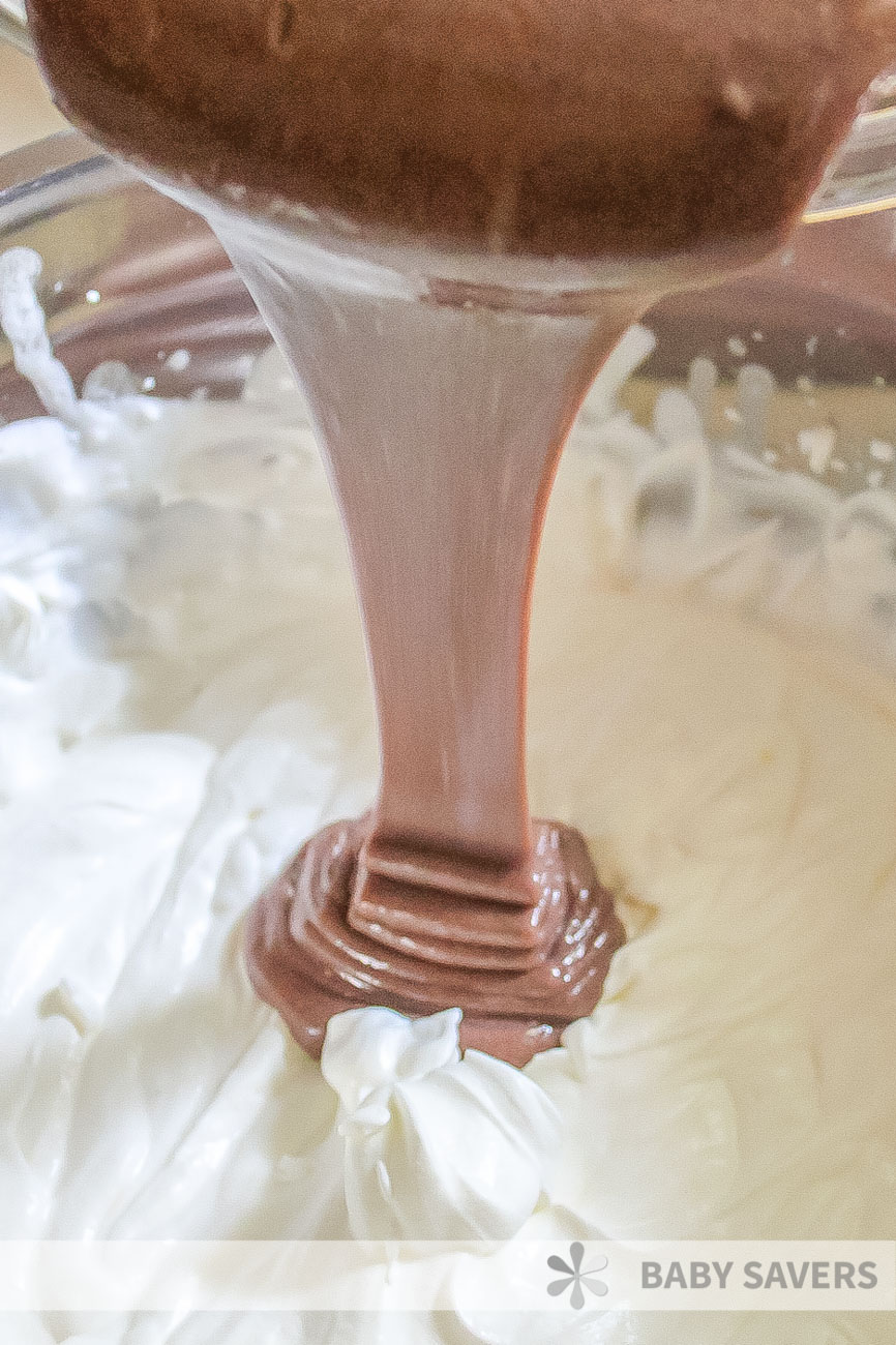 pouring chocolate pudding into a glass bowl filled with whipped cream