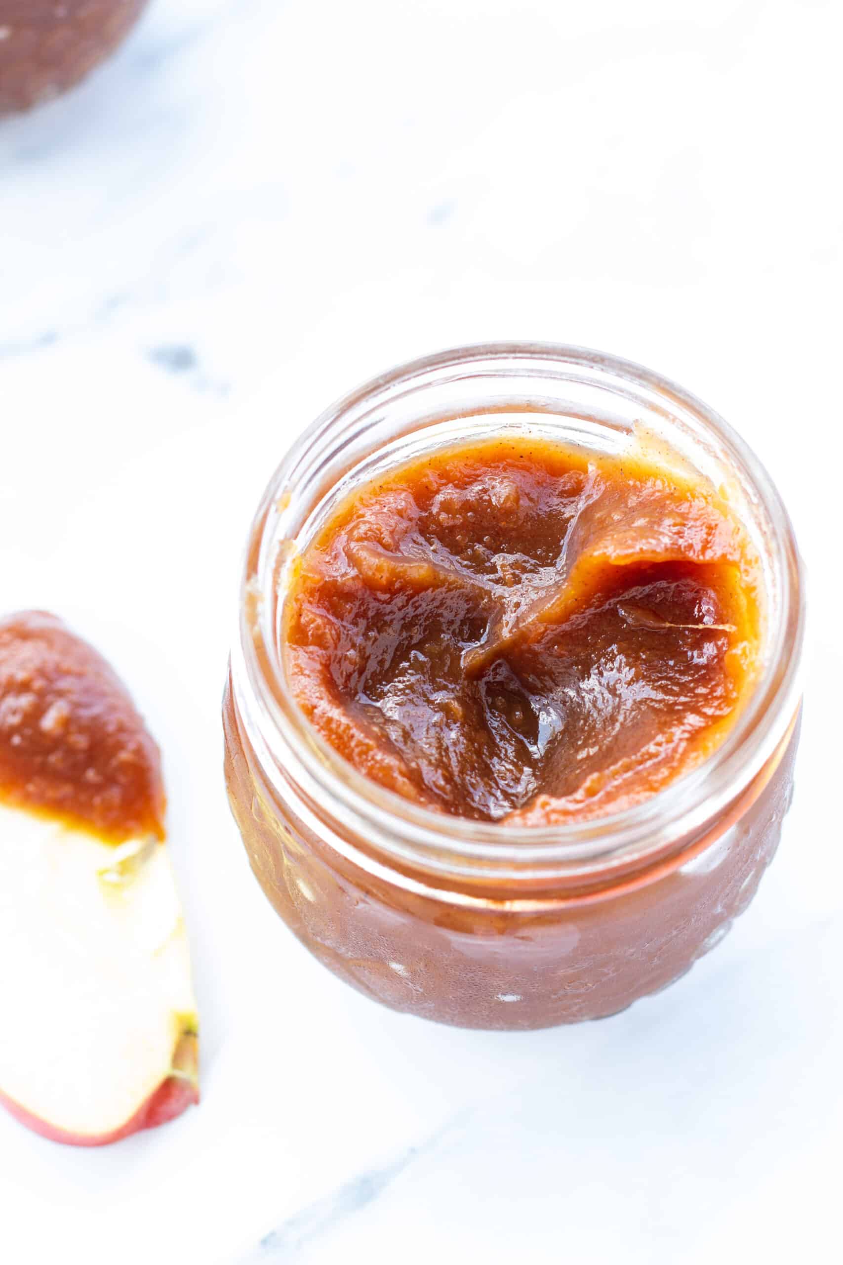 a close up of the top of apple butter in a glass jar on a white counter