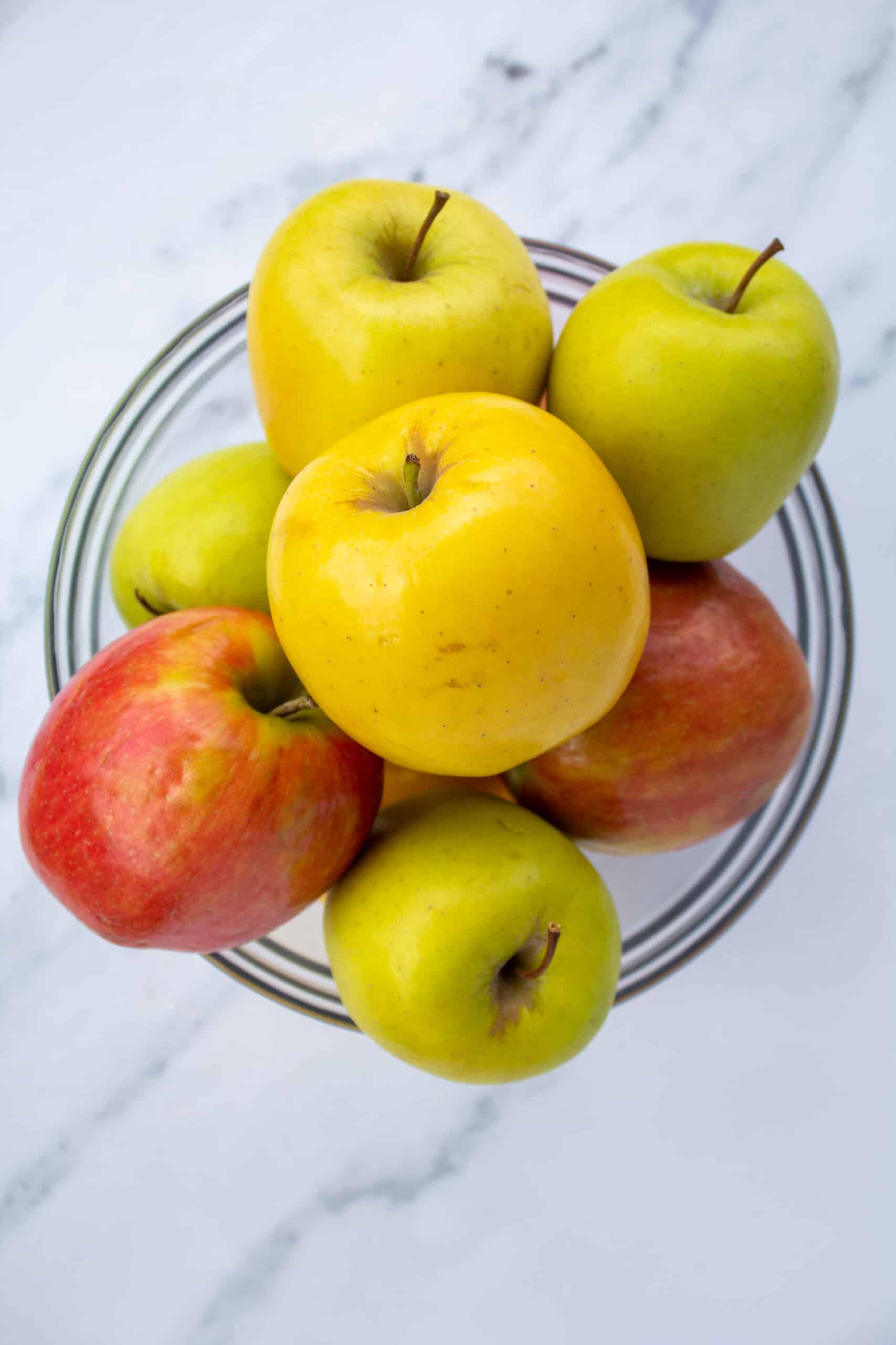 red and yellow apples in a glass bowl on a marble counter