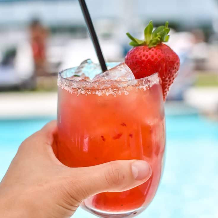 strawberry basil margarita in a hand with a whole strawberry garnish