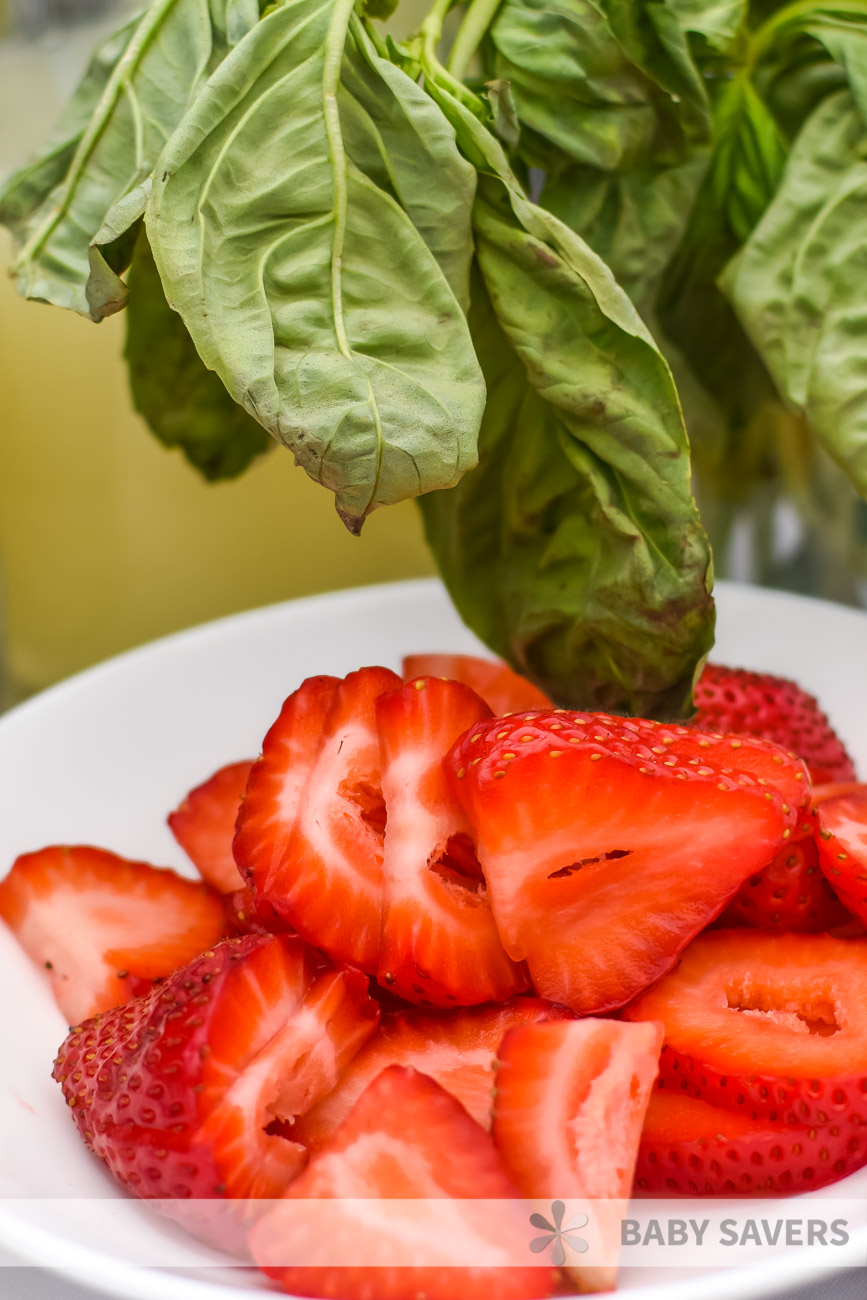 fresh basil leaves and sliced strawberries on a white plate