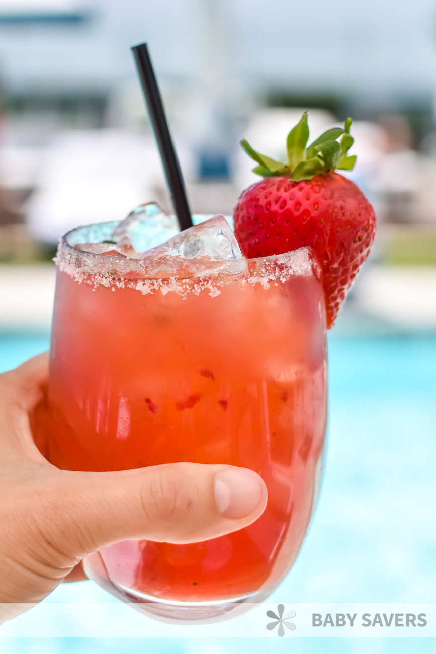 Hand holding a strawberry basil margarita with a strawberry garnish and black straw