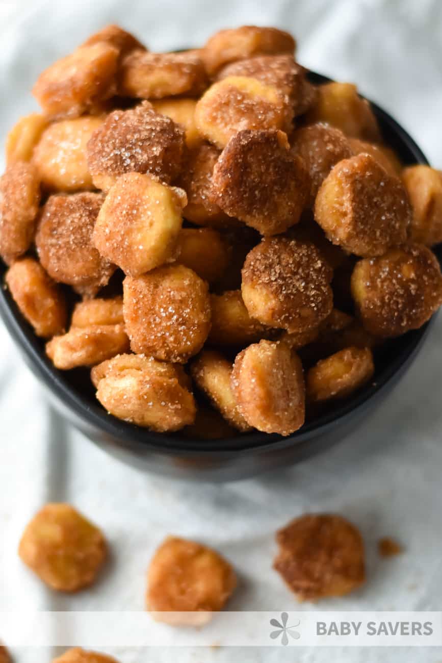 oyster cracker snack mix - a sweet and salty treat in a black bowl with more pieces spilled around the bowl