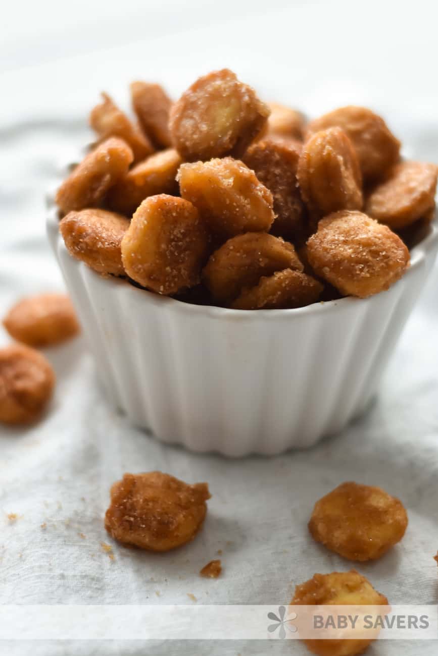 oyster cracker snack mix coated with cinnamon sugar in a white fluted dish with crackers spilled around the dish