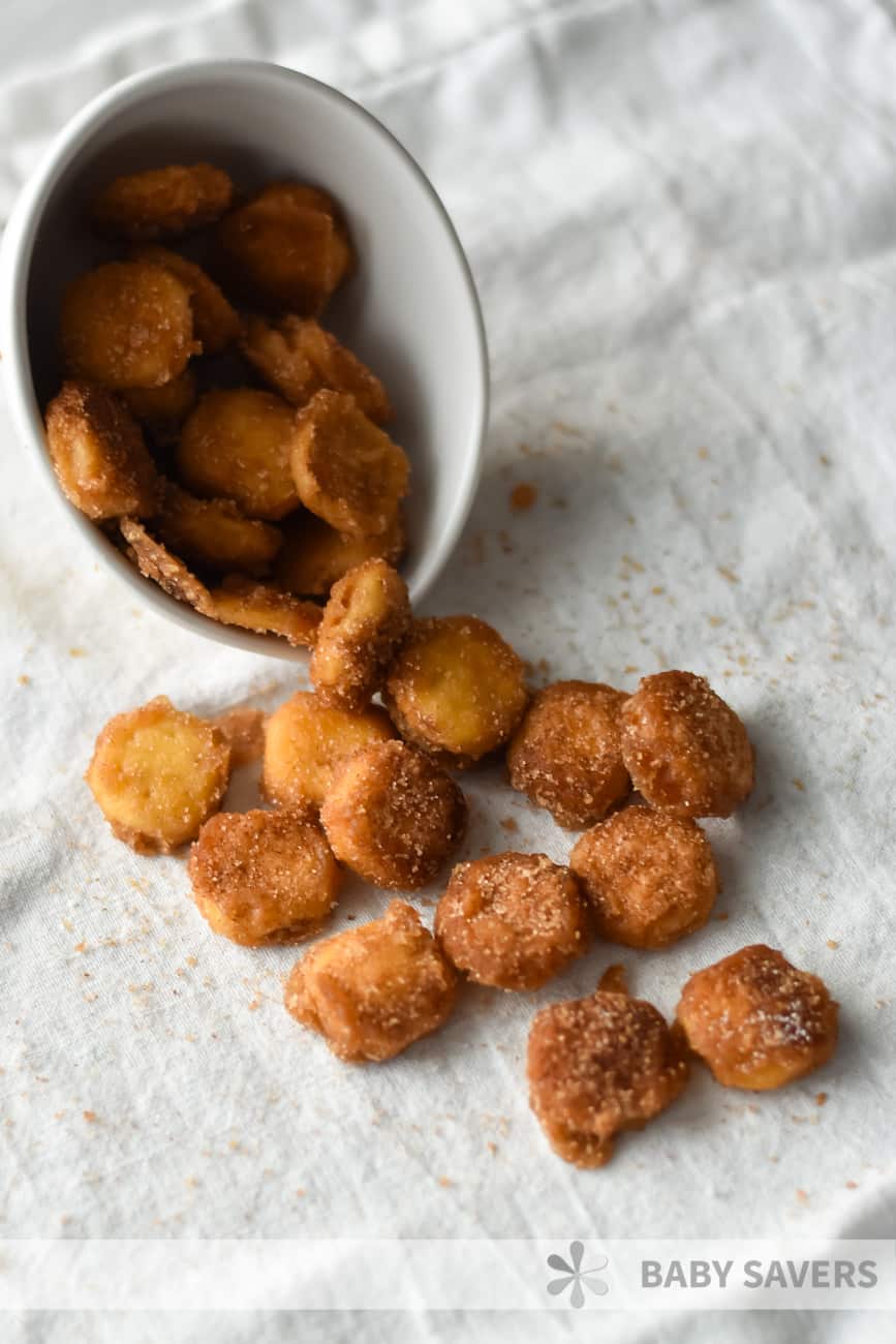 cinnamon sugar coated oyster crackers spilling out from a white bowl onto white fabric