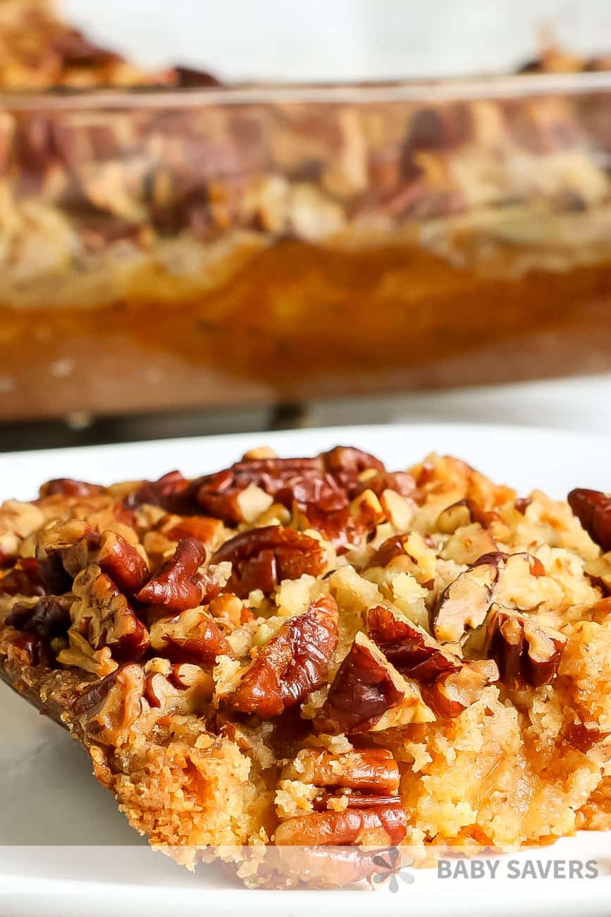 pumpkin crisp on a white plate with baking dish full of pumpkin pecan crisp behind it.