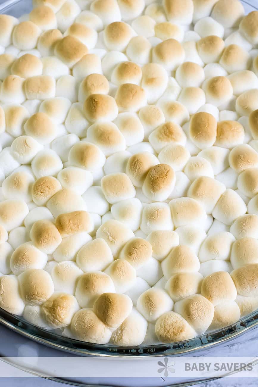 toasted marshmallows over melted milk chocolate in a baking dish