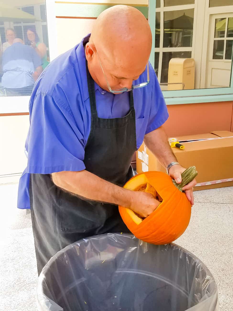man cleaning out carved pumpkin over a garbage can