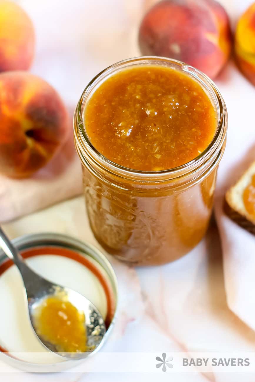 Peach butter in a glass canning jar with fresh peaches and a spoon
