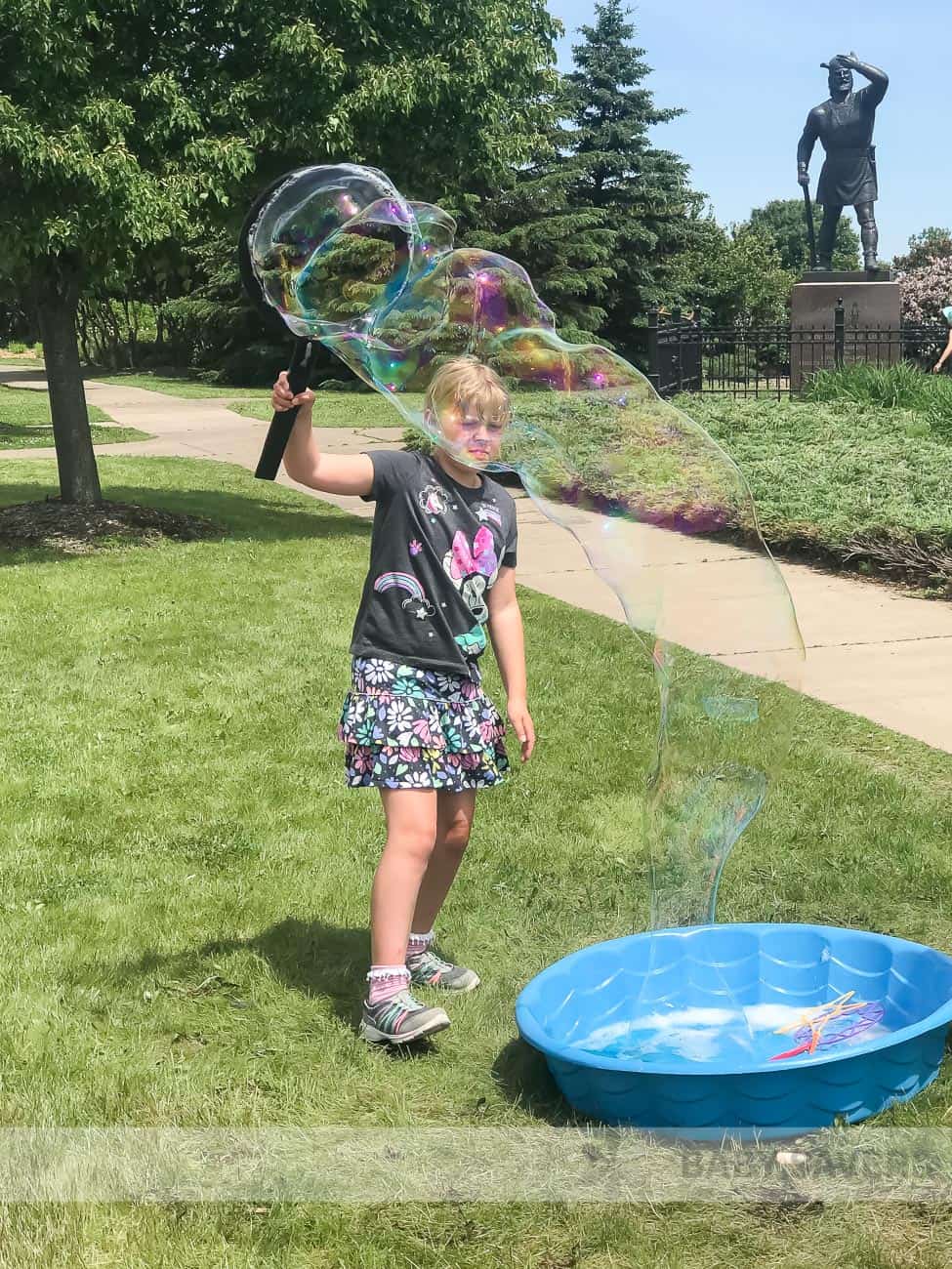 girl making a giant bubble with a tub of homemade bubble mixture