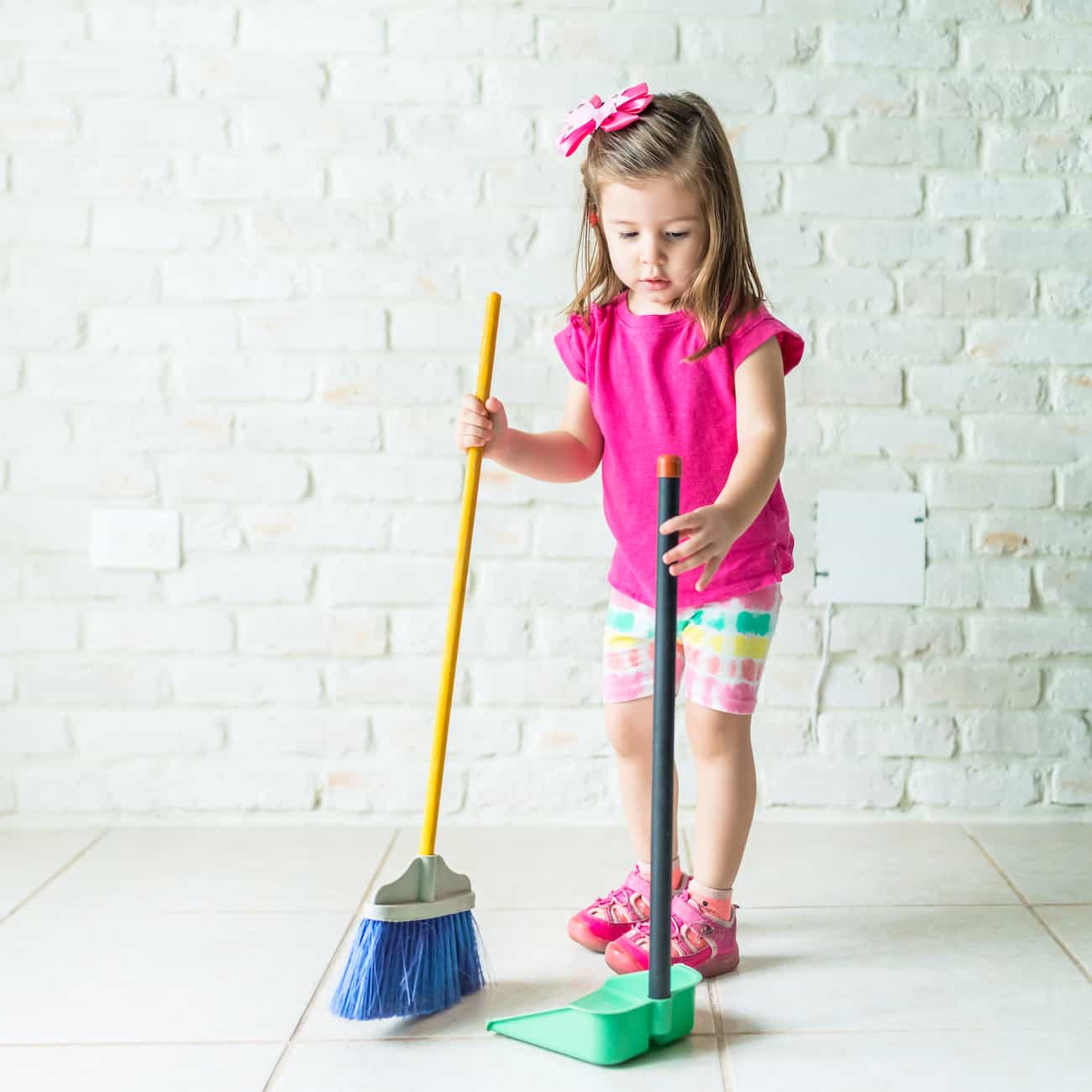 chores for kids - little girl wearing a pink shirt and sweeping