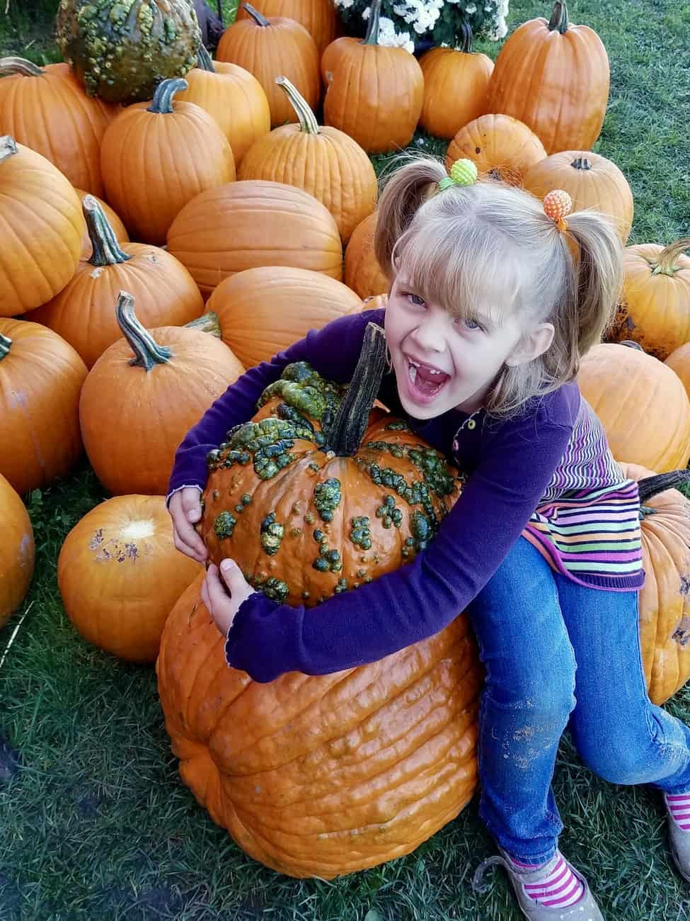 Squid Game pumpkin carving stencils post with a photo of a girl hugging a unique orange pumpkin before Halloween.