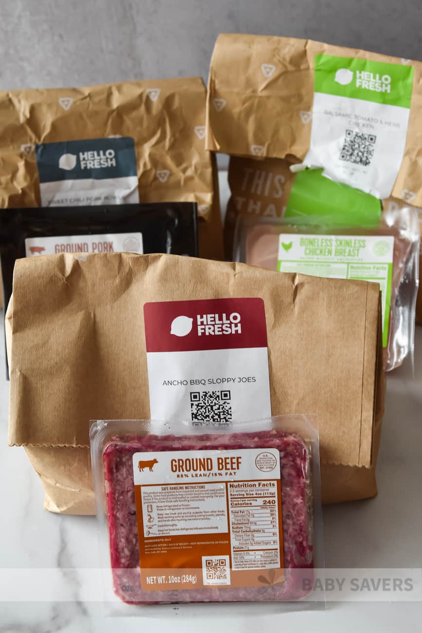 Hello Fresh Reviews - three paper bags with different meals and fresh meat in front of them.