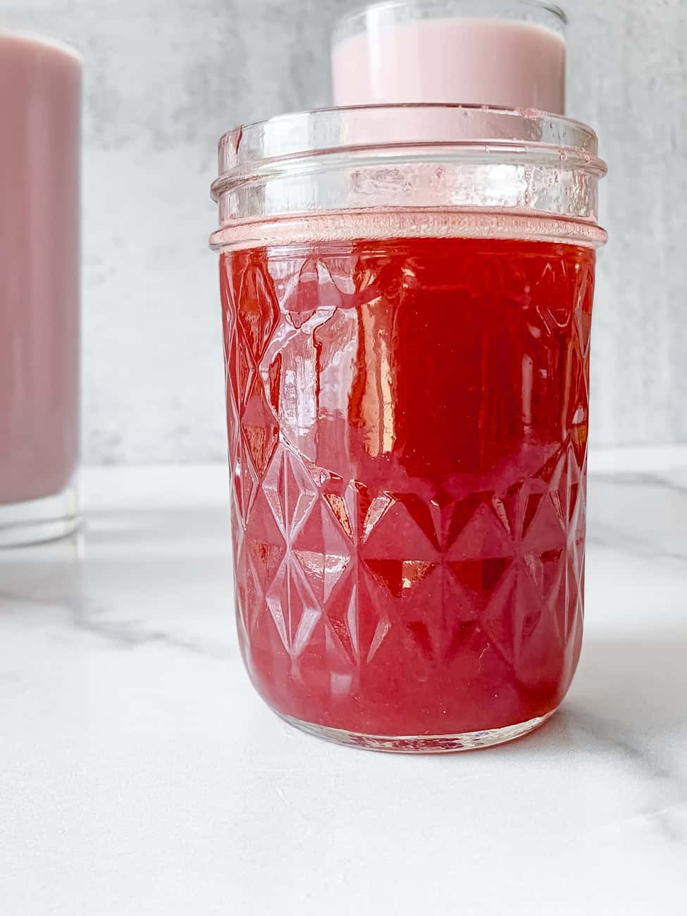 homemade Strawberry syrup recipe from scratch with two glasses of strawberry milk in the background