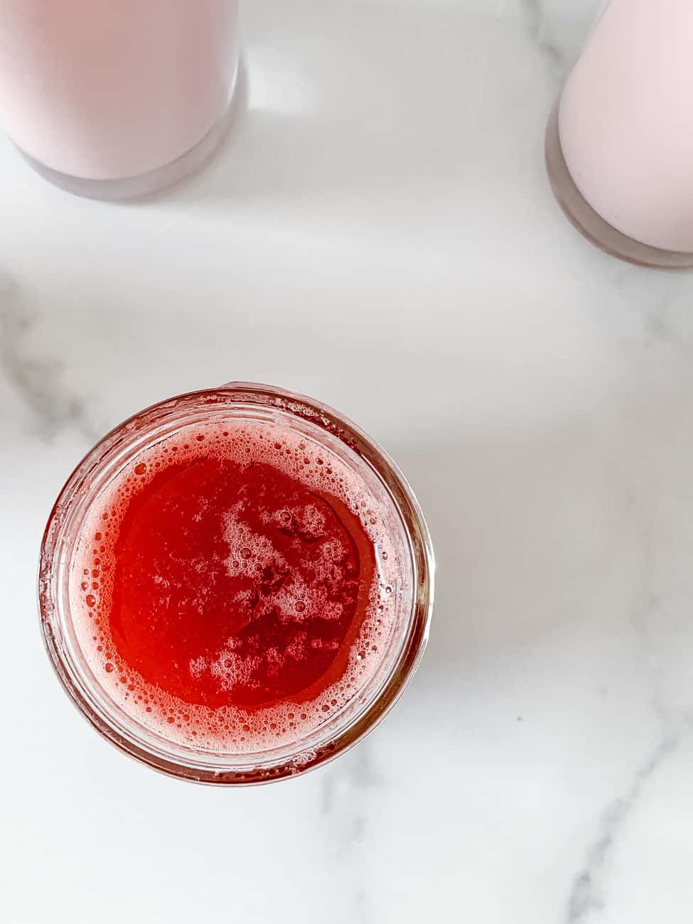 Strawberry syrup recipe stored in mason jar. Overhead shot with two glasses of homemade strawberry milk in background