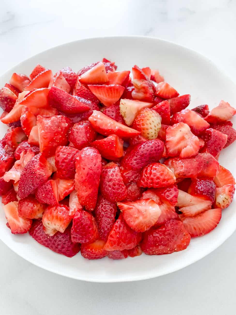 Bright red strawberries in a white bowl, cut up to use in homemade strawberry syrup