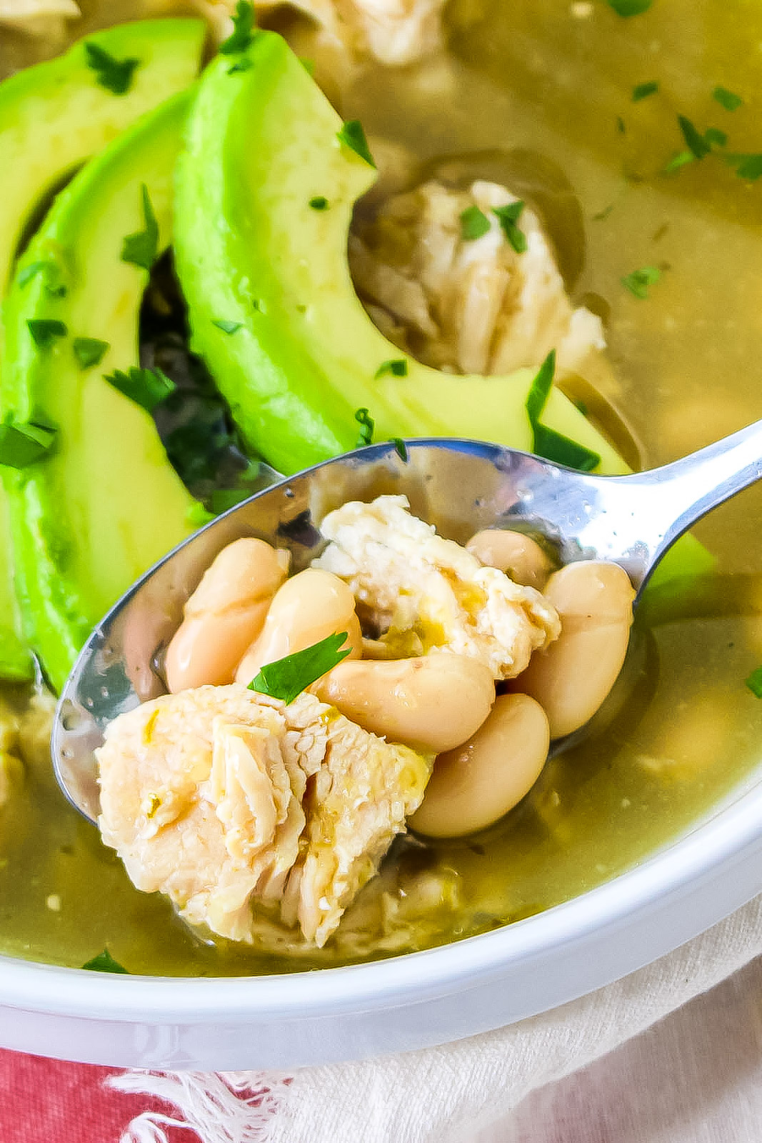 white bean chicken chili in a bowl on a red and white placemat with sliced avocado and chopped fresh cilantro