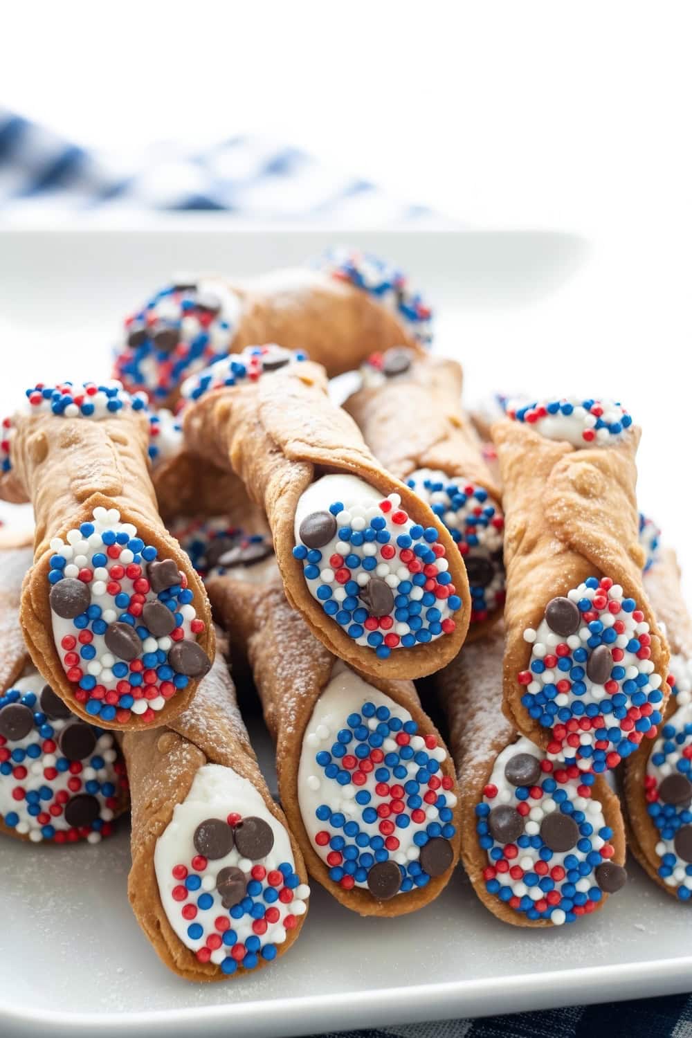 A plate of cannoli filled with cream, their ends dipped in red, white, and blue sprinkles and chocolate chips, arranged in a festive pile—perfect for Fourth of July desserts.