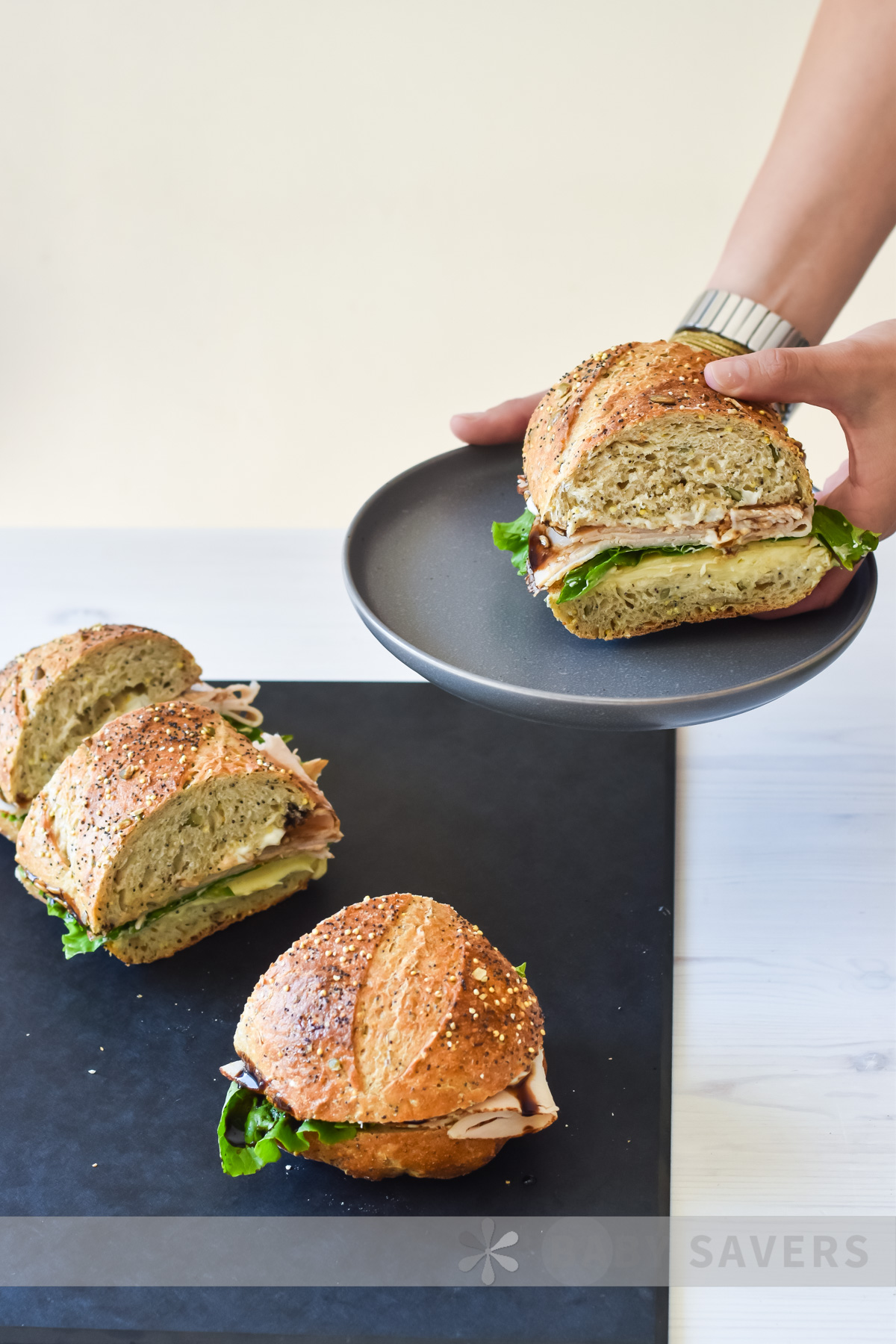 turkey sandwich recipe with hands holding a grey plate over a board with 3 other turkey sandwiches