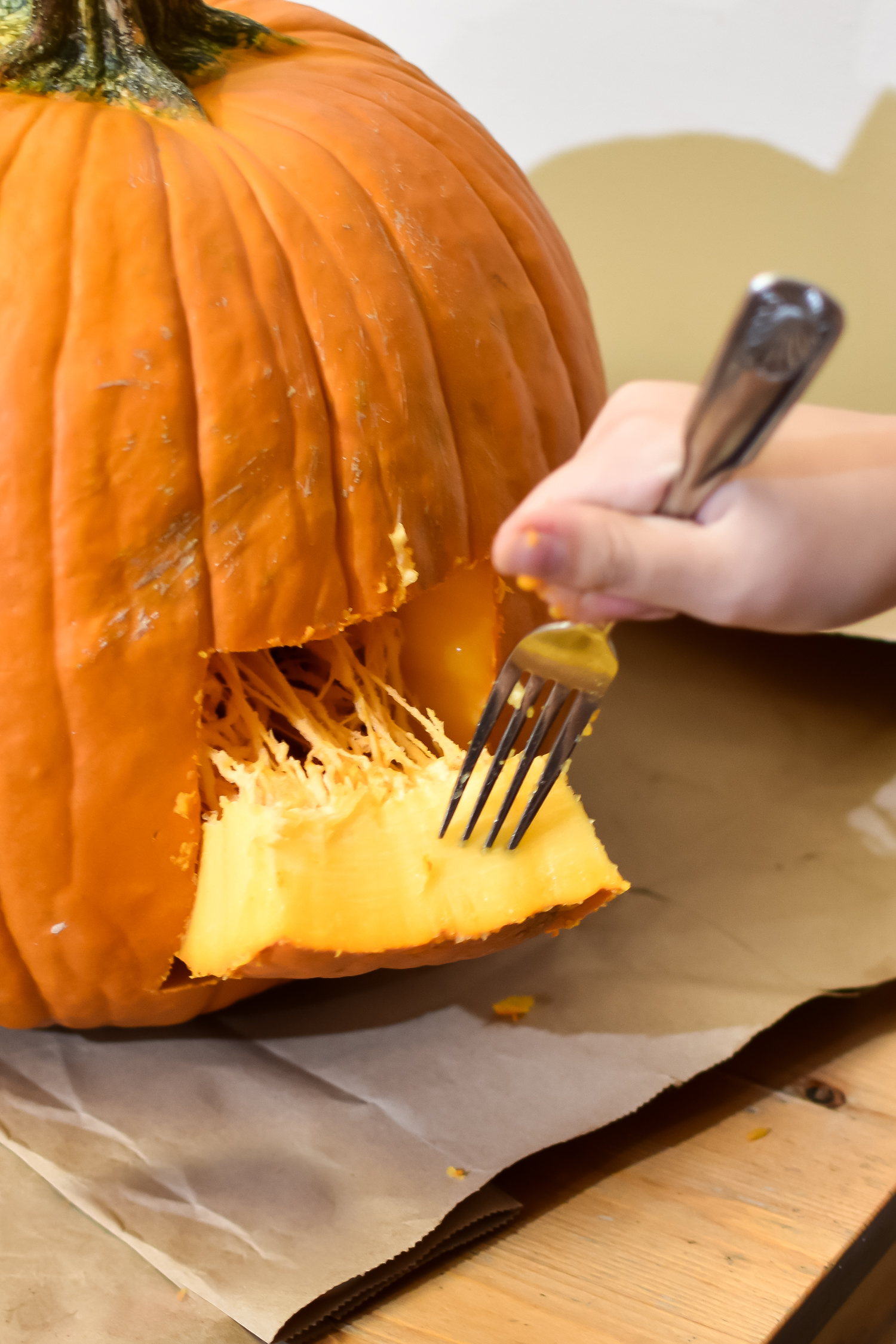 preparing a pumpkin for a cat pumpkin carving stencil by cutting a square out of the back of the pumpkin. Also shows a fork stuck in the piece of pumpkin that's cut out. 