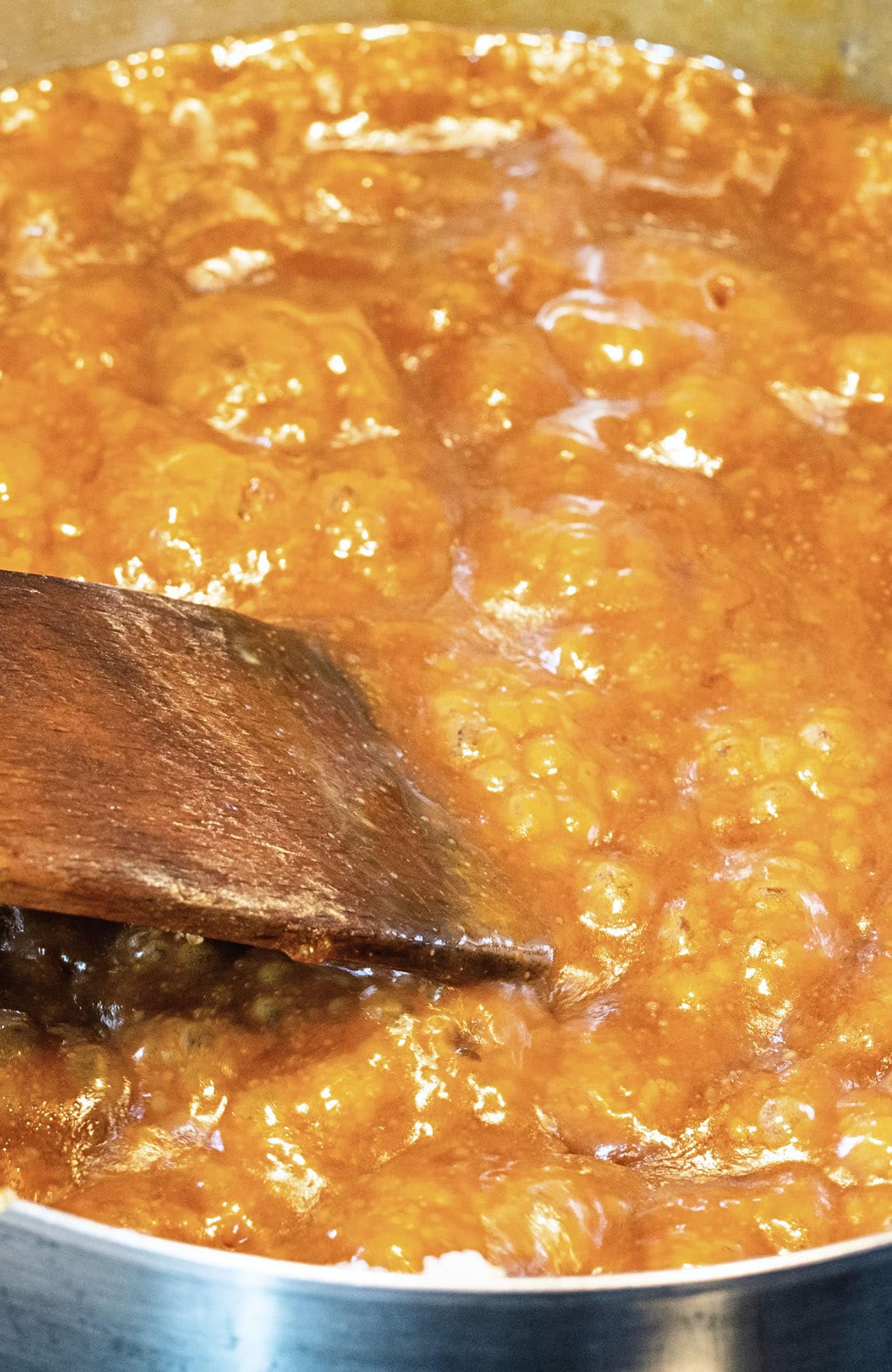 Close up of homemade caramel in the process of being made. Melted butter, brown sugar, condensed milk and corn syrup boiling in a pot with a wooden spoon stirring it. 