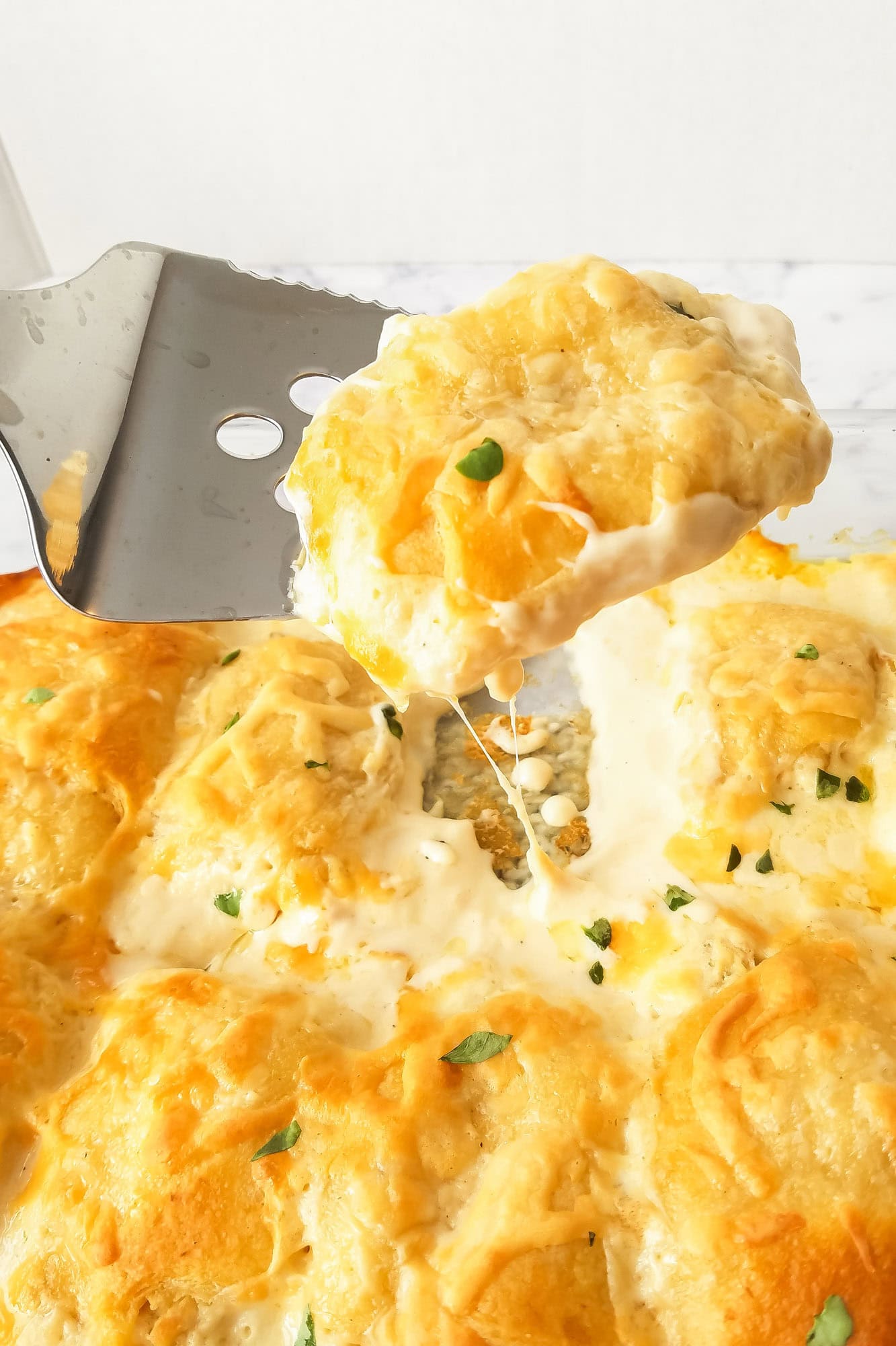 A spatula lifting a steamy slice of freshly baked chicken alfredo casserole, showing a creamy filling with chicken, wrapped with golden crescent rolls—perfect for easy dinner ideas.