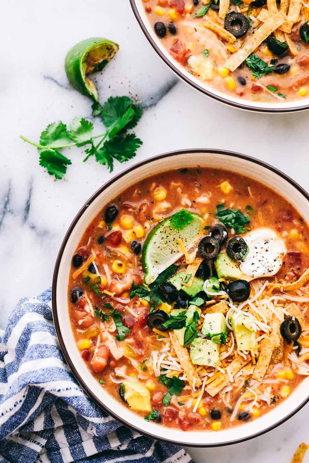 An overhead image of a vibrant 8-can chicken taco soup in a two bowls, perfect for easy dinner ideas, featuring ingredients like diced tomatoes, black beans, and corn, garnished with fresh herbs