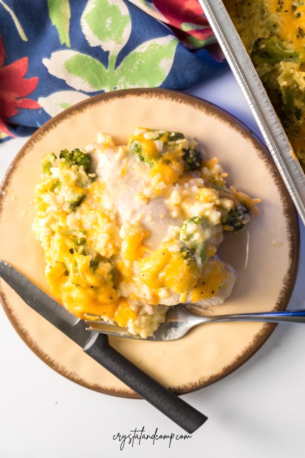 A plate of broccoli and cheese casserole with a fork on a patterned cloth napkin, ideal for busy families. The casserole is creamy with melted cheese on top, served on a
