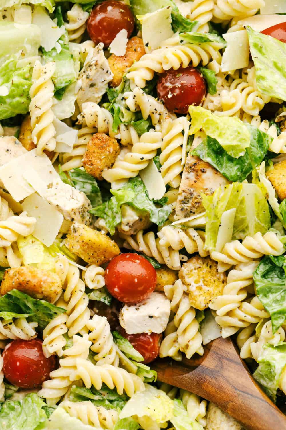 An easy dinner idea: a vibrant Caesar pasta salad with fusilli pasta, chicken, cherry tomatoes, romaine lettuce, croutons, and shaved parmesan, garnished with Caesar dressing.