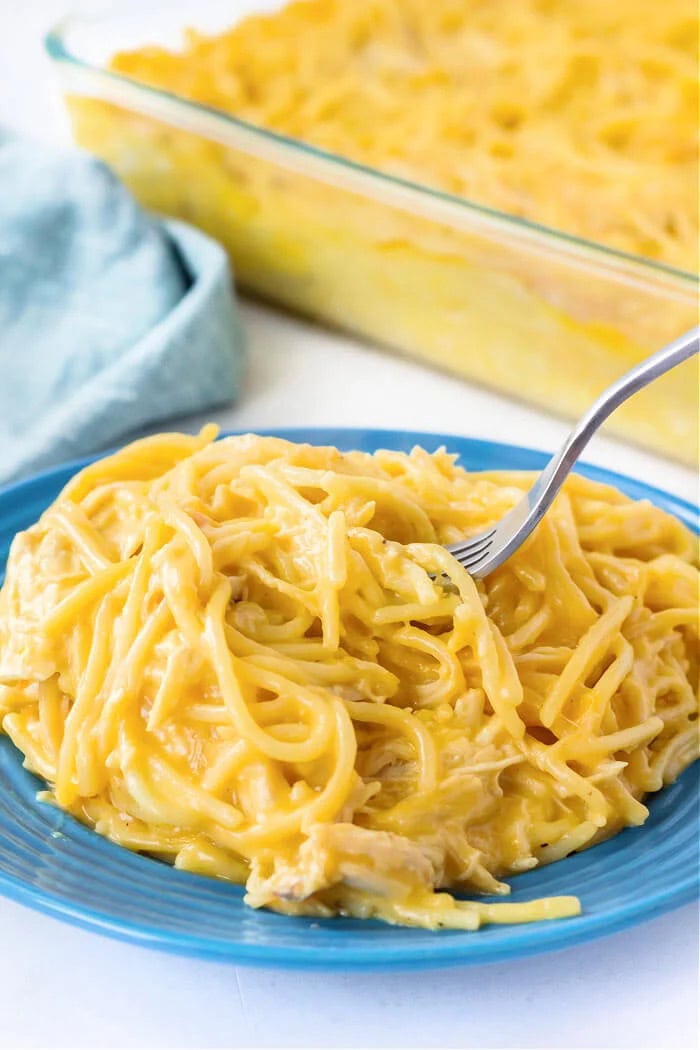 A plate of creamy spaghetti with melted cheese served on a blue plate, with a fork and a casserole dish of additional spaghetti in the background, perfect for busy families.