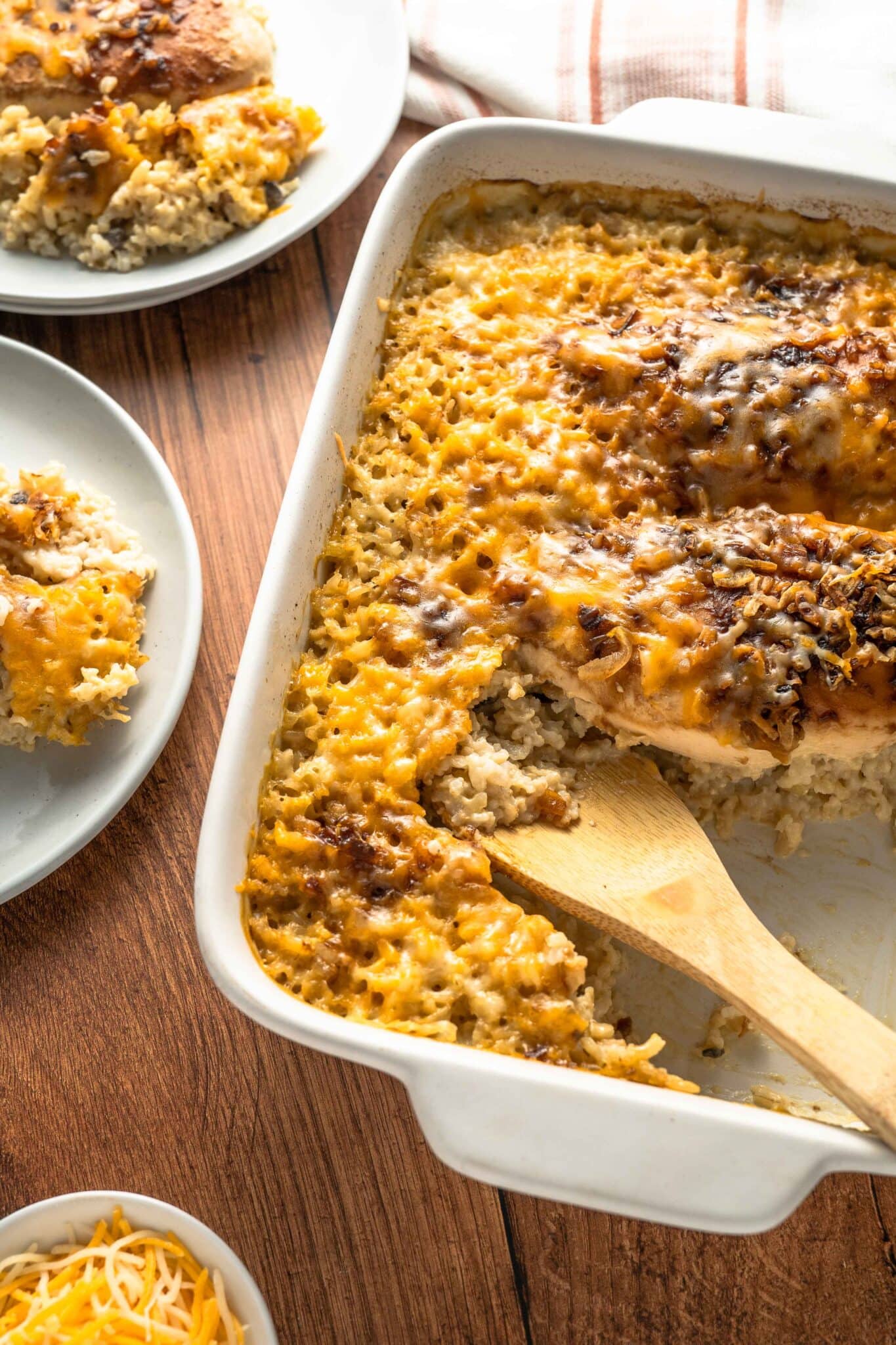 A creamy casserole dish perfect for busy families, featuring a golden-brown cheese topping, partially scooped onto white plates, with a wooden serving spoon inside the casserole dish.