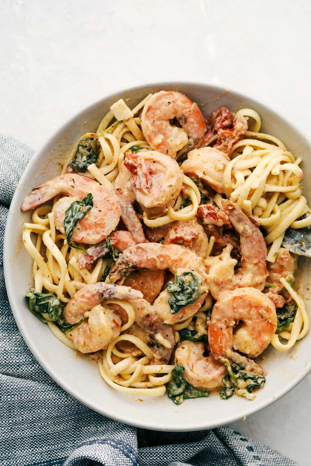 A plate of shrimp pasta, perfect as an easy dinner idea, featuring plump shrimp, linguine noodles, sun-dried tomatoes, and spinach in a creamy sauce, served on a white plate with