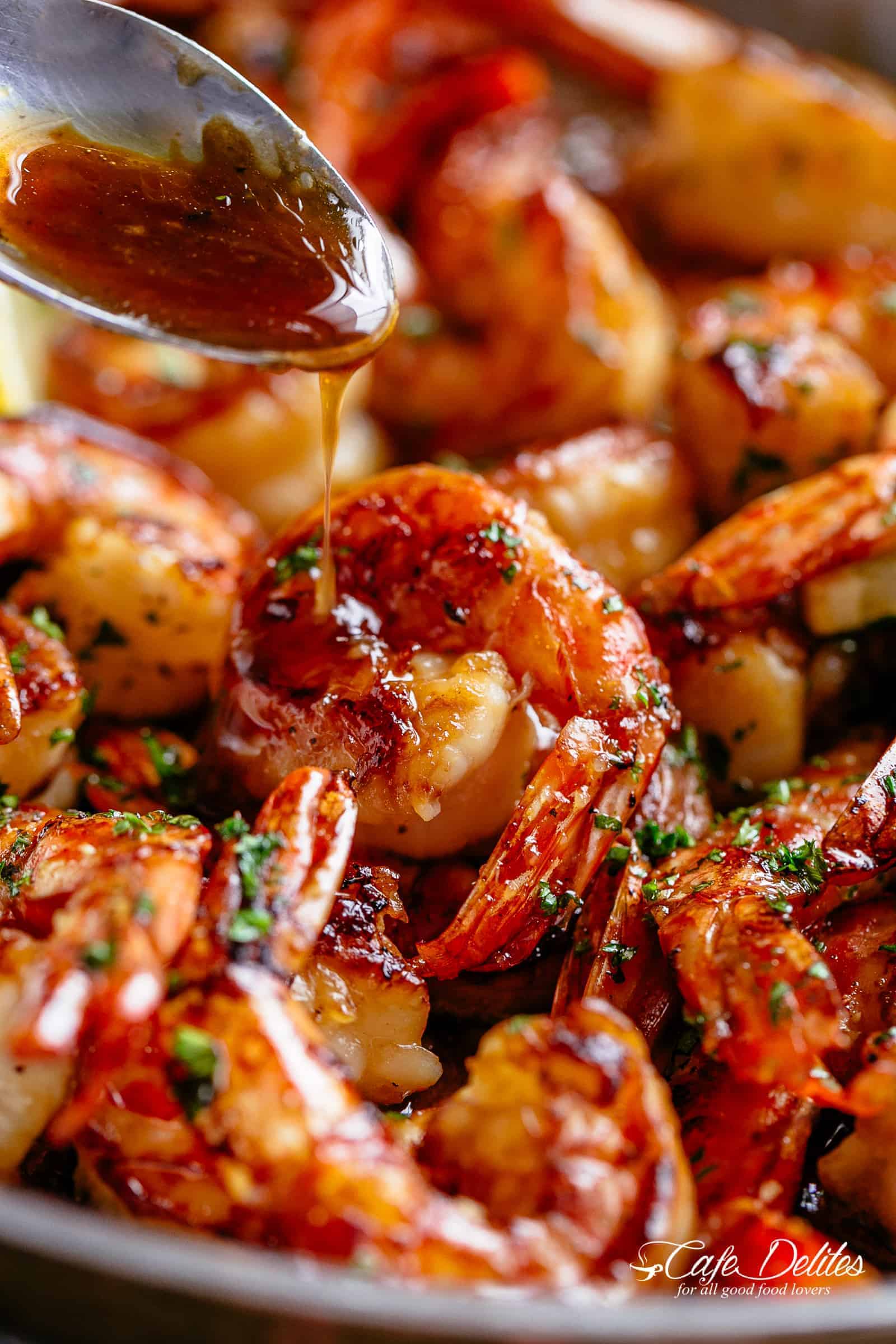 Close-up image of honey garlic shrimp garnished with herbs in a skillet, perfect for easy dinner ideas, with sauce being poured over it from a spoon.